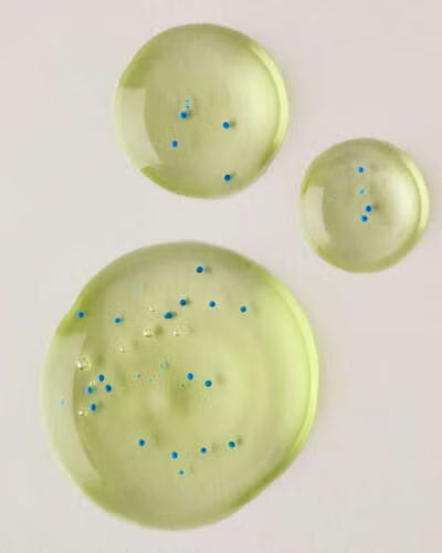 Three green round gel drops with blue specks on a light gray background