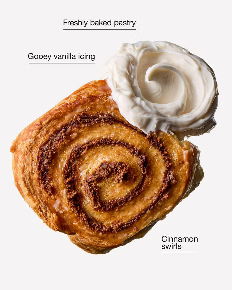 A close-up of a freshly baked pastry topped with gooey vanilla icing and a swirl of cinnamon swirl, shown on a plain light background with descriptive text labels. Purchase from www.americanbodycare.co.uk