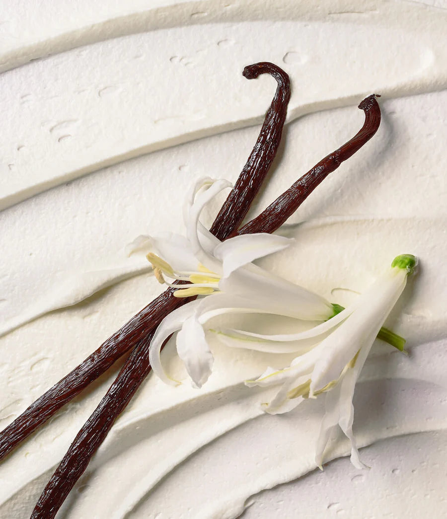 Vanilla beans and vanilla flower on a light wooden surface. Eos Cashmere body wash tube on a white background. Purchase from www.americanbodycare.co.uk