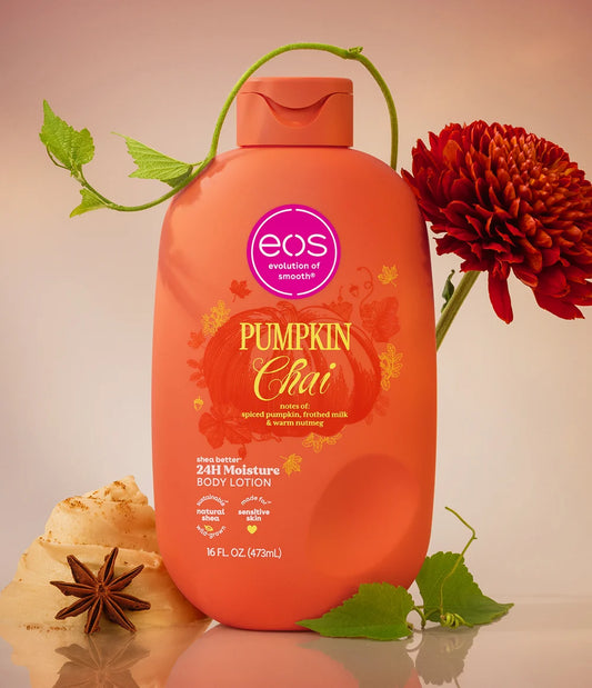 A bottle of EOS Pumpkin Chai body lotion is displayed in a styled studio setting. The bottle is bright orange with a purple EOS logo and autumn-themed graphics. purchase from www.americanbodycare.co.uk