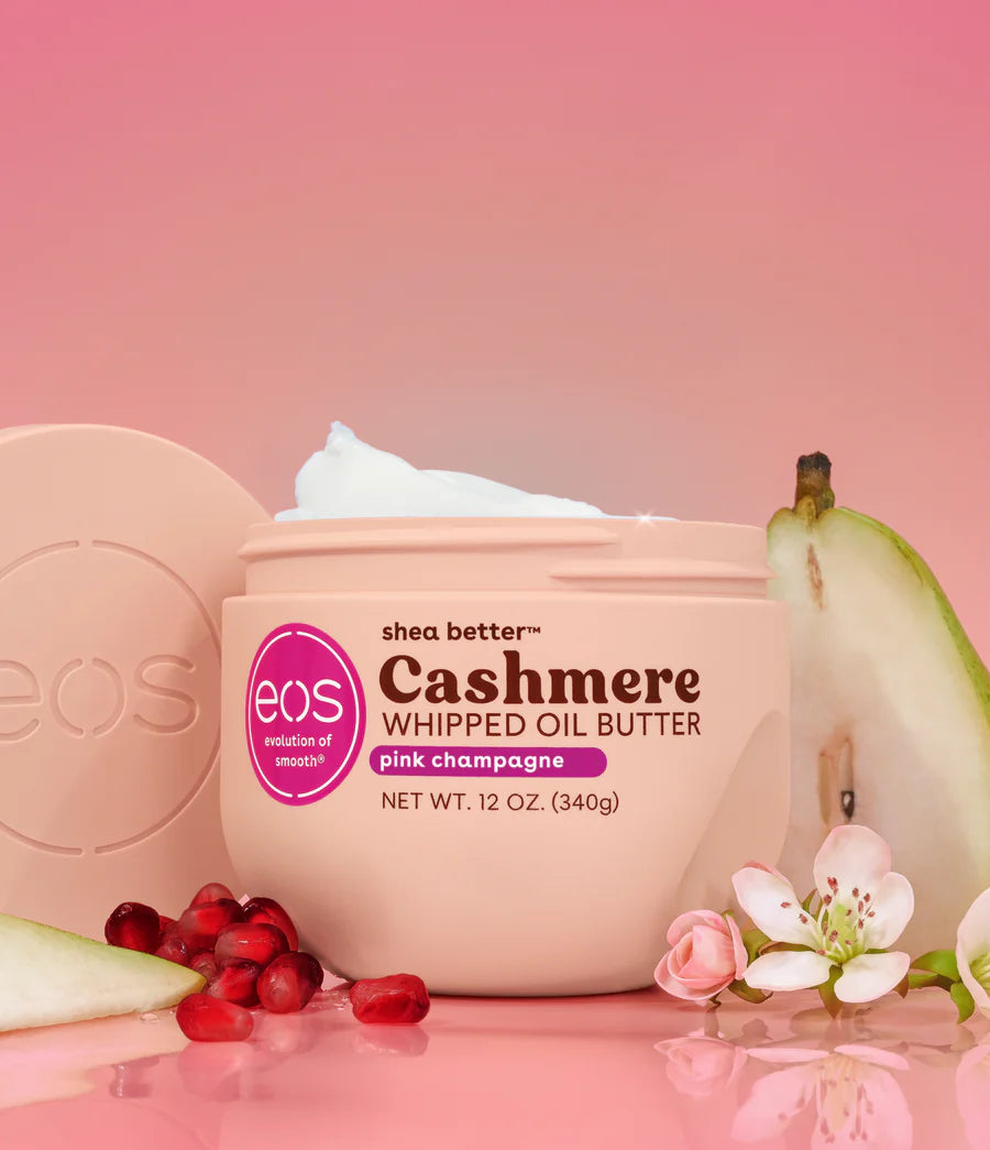 Eos Cashmere Whipped Oil Butter jar with pears, flowers, and pomegranates on a pink background. Purchase from www.americanbodycare.co.uk