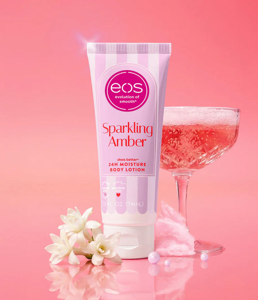 eos Sparkling Amber body lotion with a glass of sparkling wine and flowers on a pink background.Purchase from www.americanbodycare.co.uk