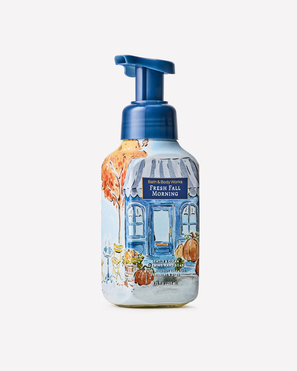 A frosted glass pump bottle of Bath & Body Works Fresh Fall Morning hand and body wash, featuring a watercolor illustration of a blue storefront with pumpkins and an orange autumn tree. Purchase from www.americanbodycare.co.uk 