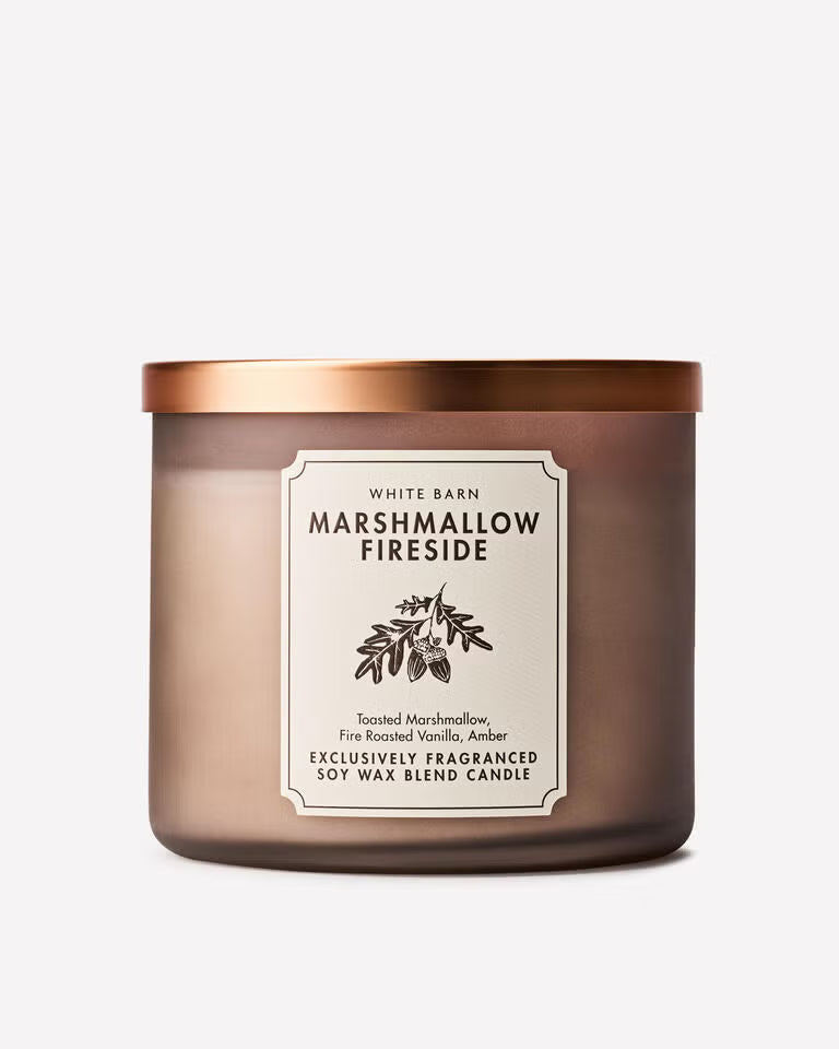 A White Barn 'Marshmallow Fireside' soy wax blend candle in a frosted amber-brown glass jar with a metallic copper lid and a cream-colored label. Purchase from www.americanbodycare.co.uk 