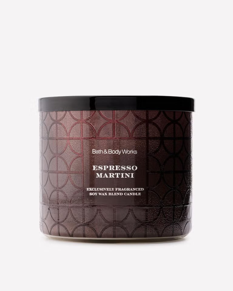 A Bath & Body Works Espresso Martini scented wax blend candle in a cylindrical jar with a black lid and a dark brown patterned label, set against a plain light gray background. Purchase from www.americanbodycare.co.uk 