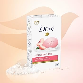 A box of Dove rebalancing soap bars with a pink bar of soap and peach illustration on the front, shown on a soft peach background with a few soap bubbles in the foreground. Purchase from www.americanbodycare.co.uk 