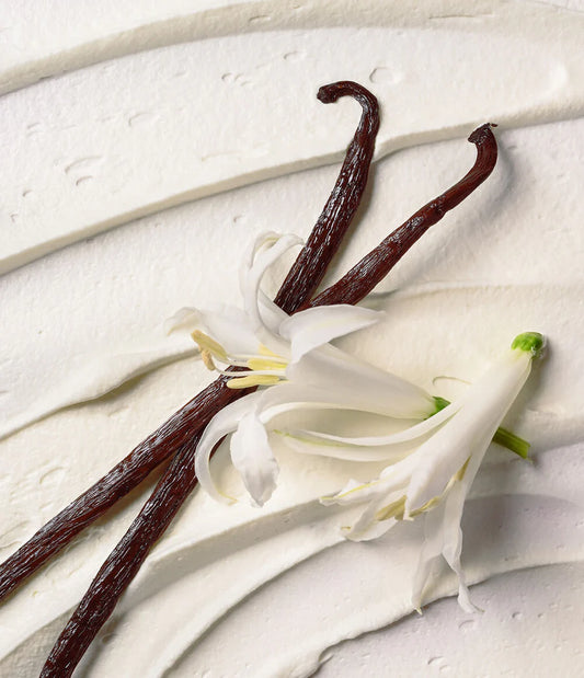 Vanilla beans and vanilla flower on a light wooden surface. Eos Cashmere body wash tube on a white background. Purchase from www.americanbodycare.co.uk 