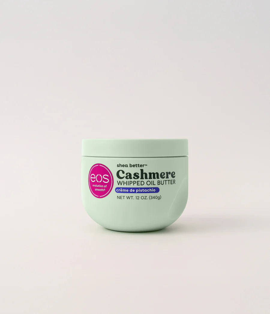 A light mint green jar of EOS Cashmere Whipped Oil Butter with a pink circular logo, centered on a light gray background. Purchase from www.americanbodycare.co.uk 