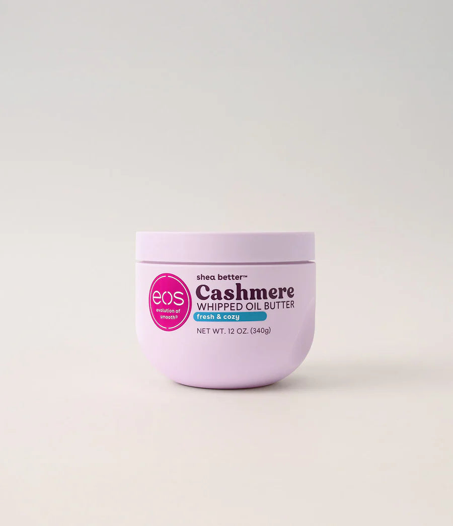 A 12 oz jar of EOS Cashmere Whipped Oil Butter in Pink & Blue, featuring a light lavender-purple container with a pink circular logo and black text, set against a clean, light off-white background. Purchase from www.americanbodycare.co.uk 