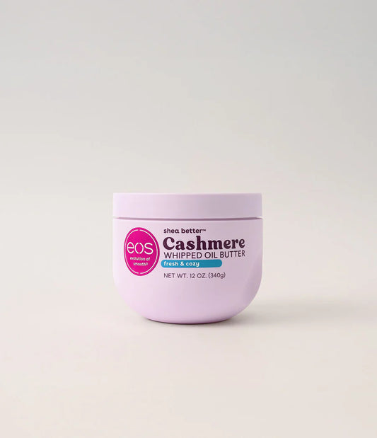 A 12 oz jar of EOS Cashmere Whipped Oil Butter in Pink & Blue, featuring a light lavender-purple container with a pink circular logo and black text, set against a clean, light off-white background. Purchase from www.americanbodycare.co.uk 