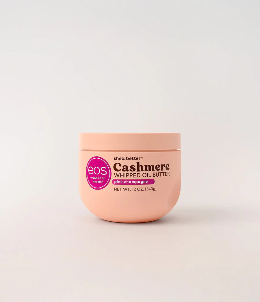 A 12 oz jar of EOS Shea Better Cashmere Whipped Oil Butter in a soft peach-pink color, set against a clean white background. Purchase from www.americanbodycare.co.uk 
