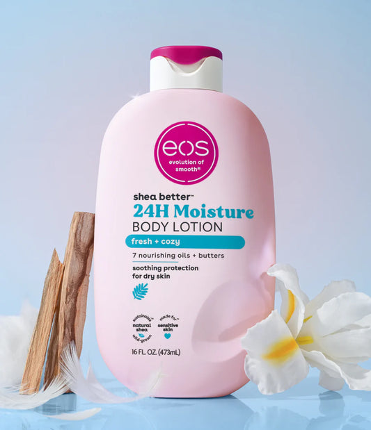 Pink bottle of eos 24H Moisture Body Lotion on a light blue background with flowers and wooden elements. Purchase from www.americanbodycare.co.uk 