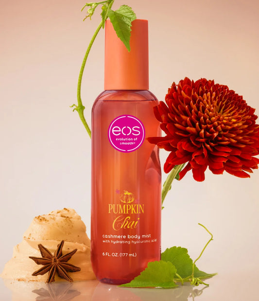 EOS Cosmetics Chai Pumpkin Cashmere Body Mist in a clear bottle showing the orange liquid inside, styled with a red flower, star anise, and ginger on a warm beige background. www.americanbodycare.co.uk