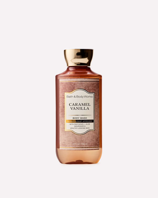 A bottle of Bath & Body Works Caramel Vanilla body wash, featuring a warm amber-brown liquid inside a clear bottle with a metallic gold cap and a cream-colored label, set against a solid light gray background. purchase from www.americanbodycare.co.uk