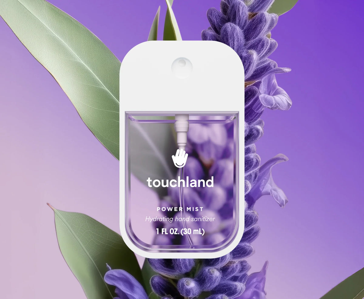 Touchland power mist bottle surrounded by lavender flowers and leaves on a purple background. Purchase from www.americanbodycare.co.uk
