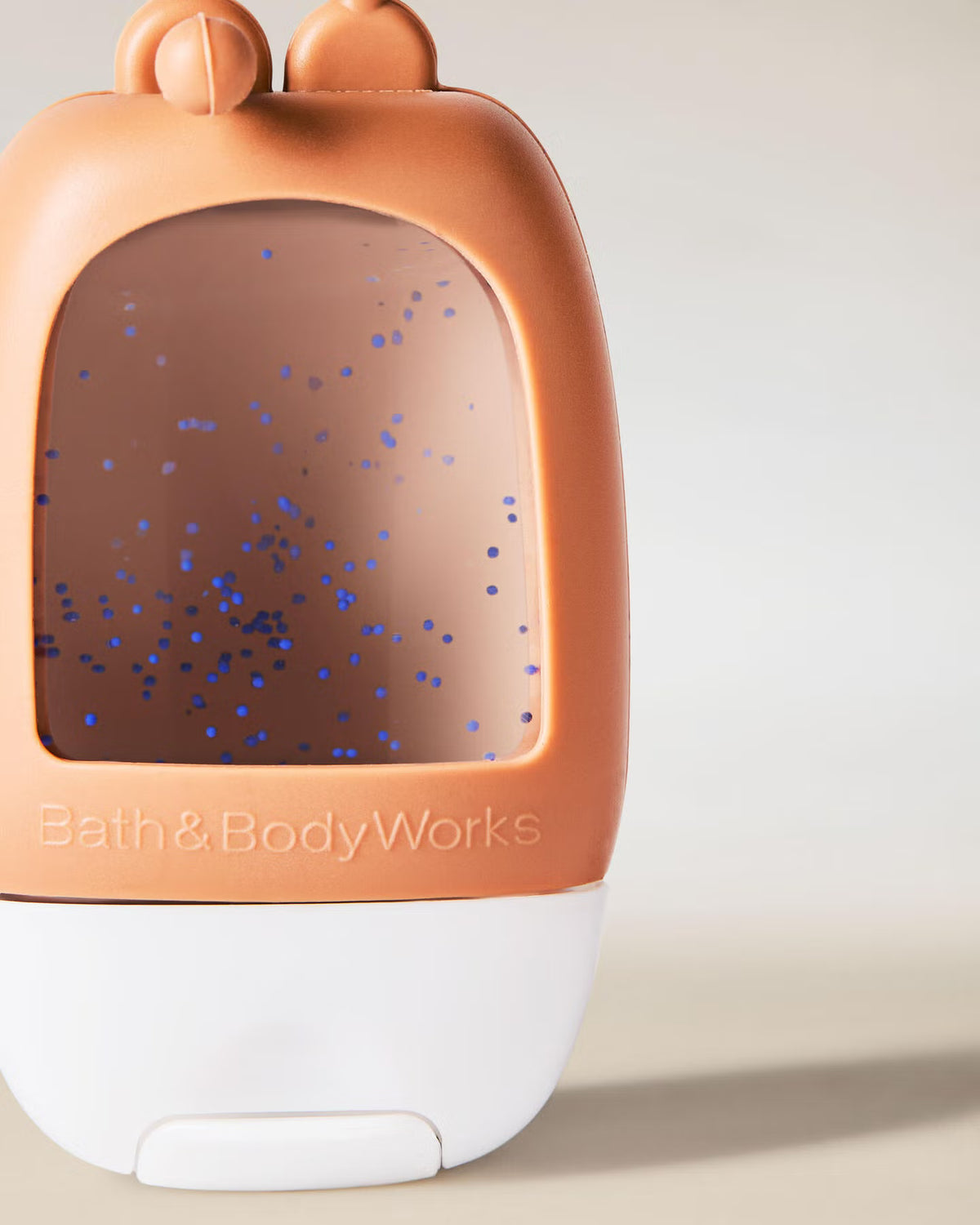 Handheld diffuser with a brown top and white base, featuring 'Bath & Body Works' branding, on a light background. A Bath Body Works hand sanitizer bottle with a brown cap and strap, featuring a clear window showing a speckled amber liquid, on a light gray background. purchase from www.americanbodycare.co.uk