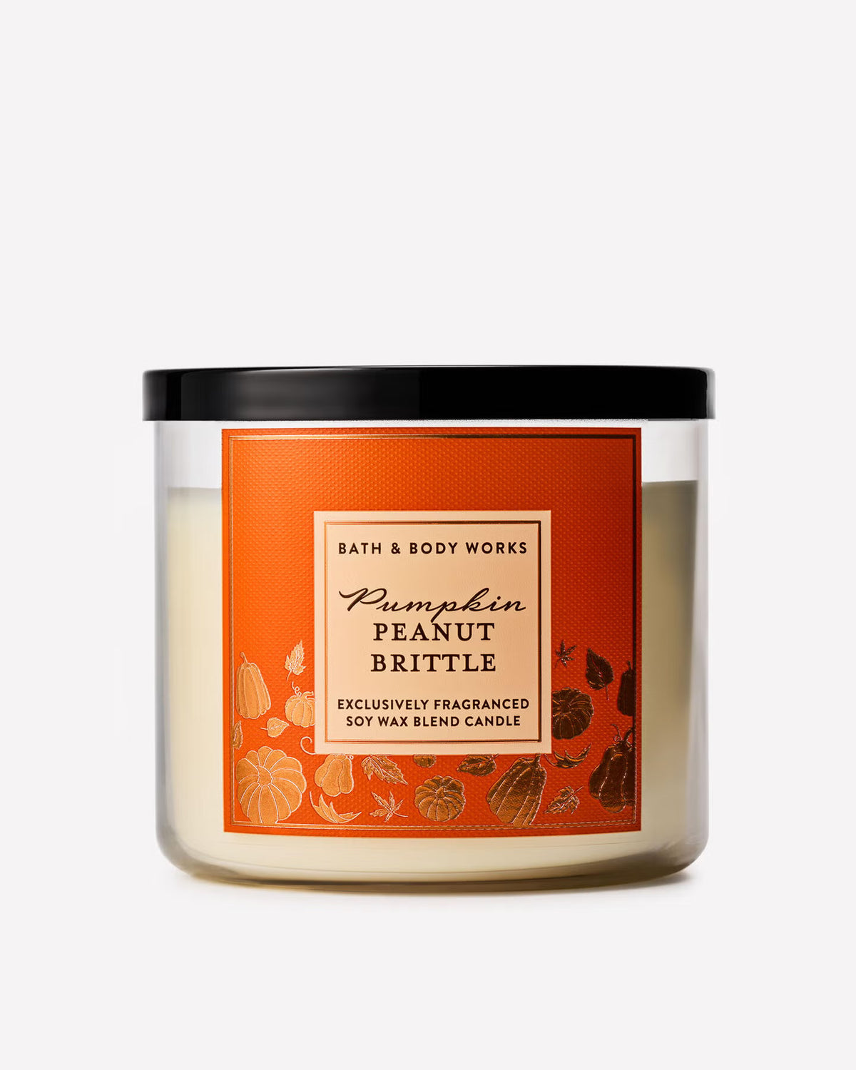 A Bath & Body Works 'Pumpkin Peanut Brittle' soy wax blend candle in a clear glass jar with a black lid and a prominent orange label featuring autumn-themed illustrations. Purchase from www.americanbodycare.co.uk