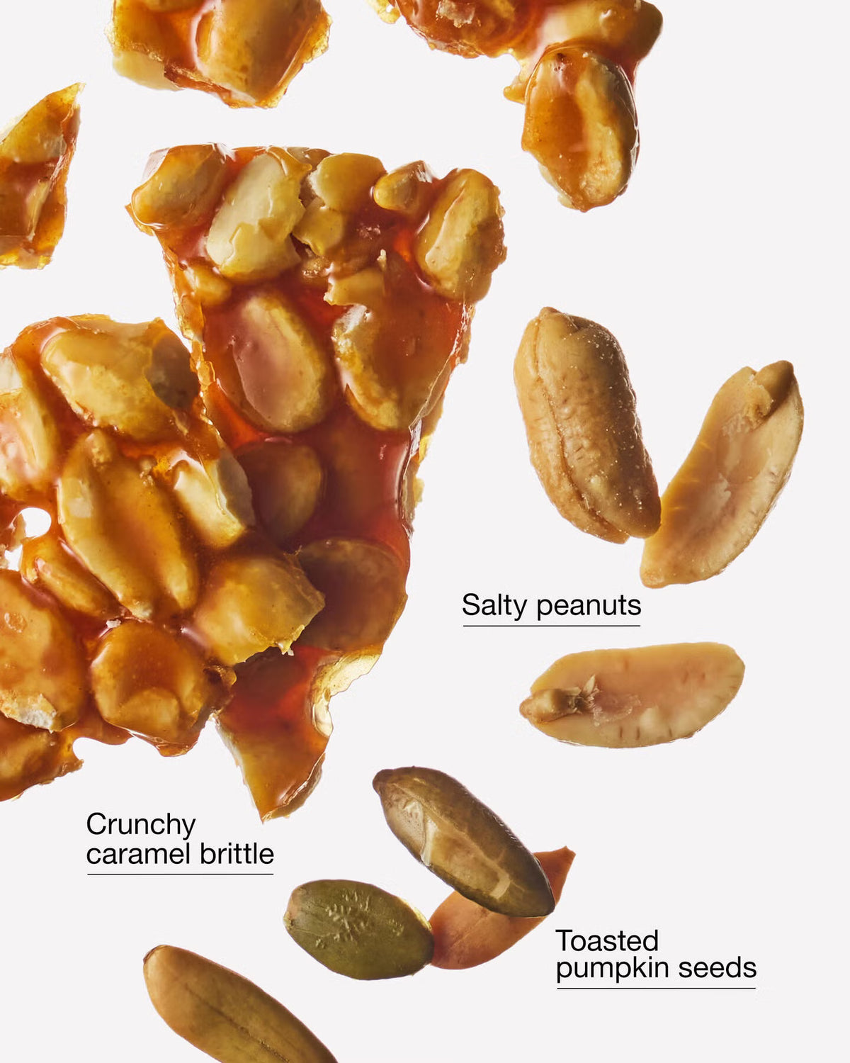 A close-up studio shot of peanut brittle with whole peanuts and toasted pumpkin seeds floating on a white background, with text labels reading 'Salty peanuts,' 'Crunchy caramel brittle,' and 'Toasted pumpkin seeds.'. A Bath & Body Works 'Pumpkin Peanut Brittle' soy wax blend candle in a clear glass jar with a black lid and a prominent orange label featuring autumn-themed illustrations. Purchase from www.americanbodycare.co.uk
