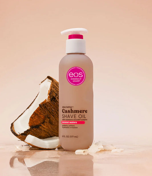 Bottle of eos Cashmere Shave Oil with a coconut on a beige background. Purchase from americanbodycare.co.uk 