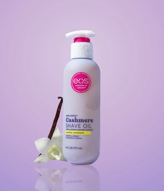 Bottle of eos Cashmere Shave Oil on a purple background with vanilla bean and orchid. Purchase from americanbodycare.co.uk