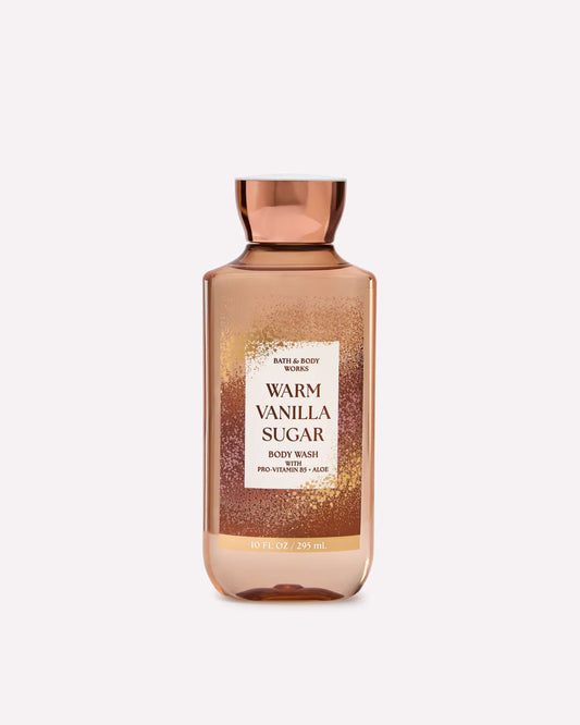 A bottle of Bath & Body Works Warm Vanilla Sugar body wash with a metallic rose gold cap and a glittery rose gold label, shown on a light gray background. purchase from www.americanbodycare.co.uk
